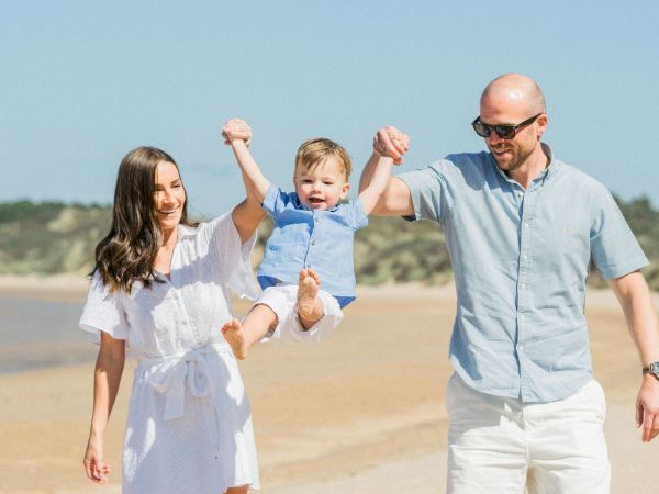 A happy family on a sunny beach: parents hold a giggling baby as they play in the sand.