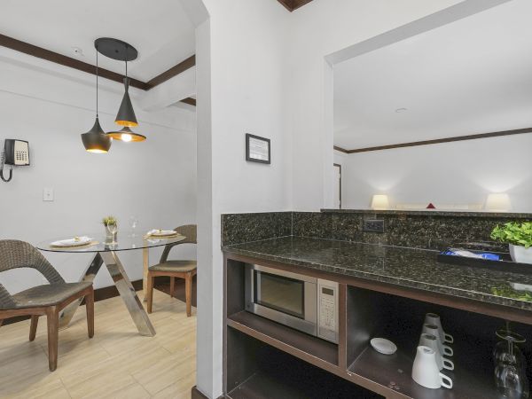 Modern indoor space with a dining table, pendant lights, and a kitchen counter with stove and coffee maker.