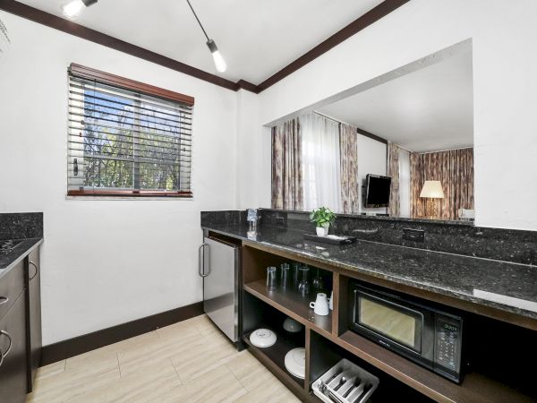 Bright modern kitchen with black granite counters, sink, built-in oven, stovetop, cabinets, and curtained windows by a dining nook.