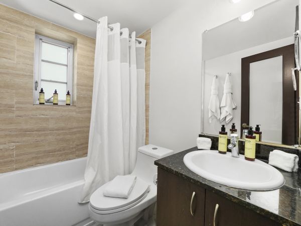 A clean bathroom with a bathtub, toilet, white shower curtain, and a vanity sink stocked with toiletries.