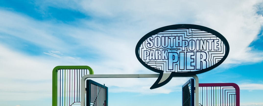 A wooden pier over the ocean with a sign reading &ldquo;South Pointe Park Pier&rdquo; and people walking under a blue sky.