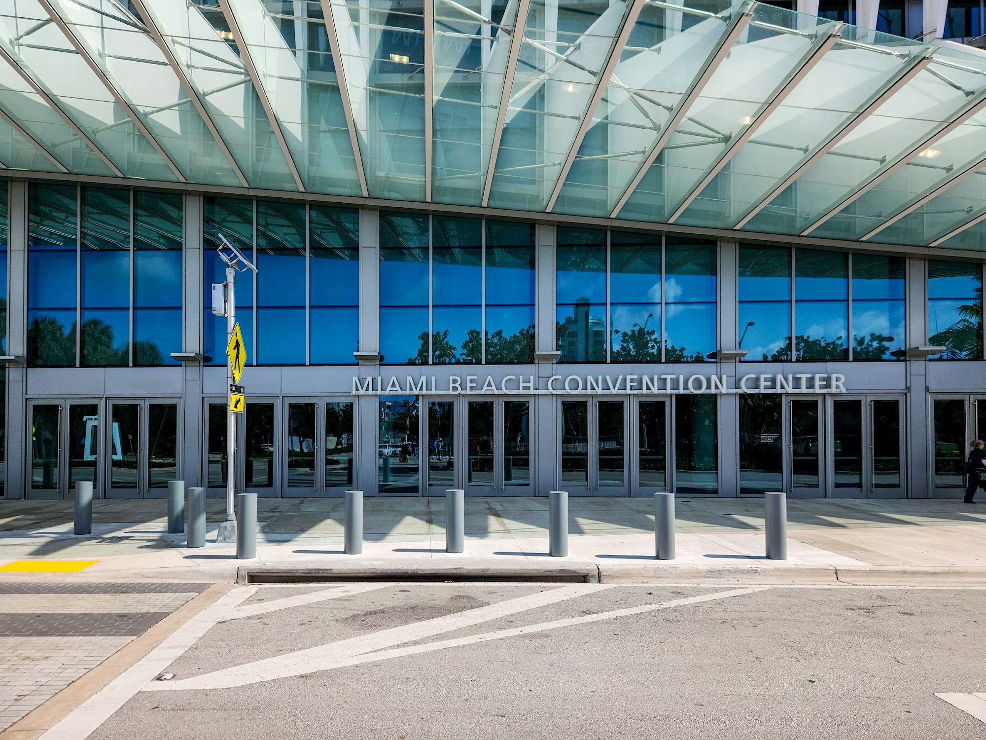 The Miami Beach Convention Center entrance is shown with a glass facade, large windows, and the building name on the wall.