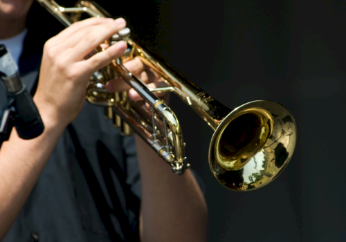 A musician plays a shiny brass trumpet, holding it up while sounding notes under stage lighting.
