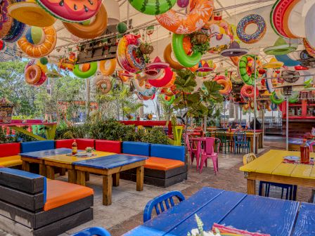 A colorful outdoor restaurant patio with hanging inflatable decorations, party lights, and bright tables and seating.